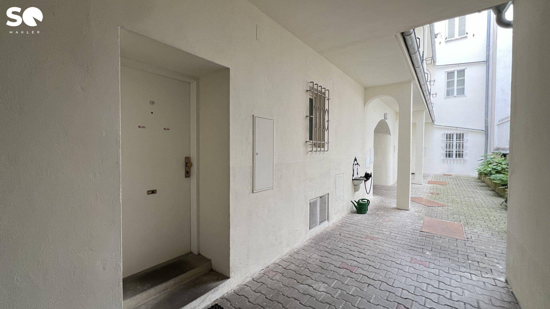 Eingangsbereich im Innenhof mit gepflastertem Boden und Zugang zur Wohnung.
