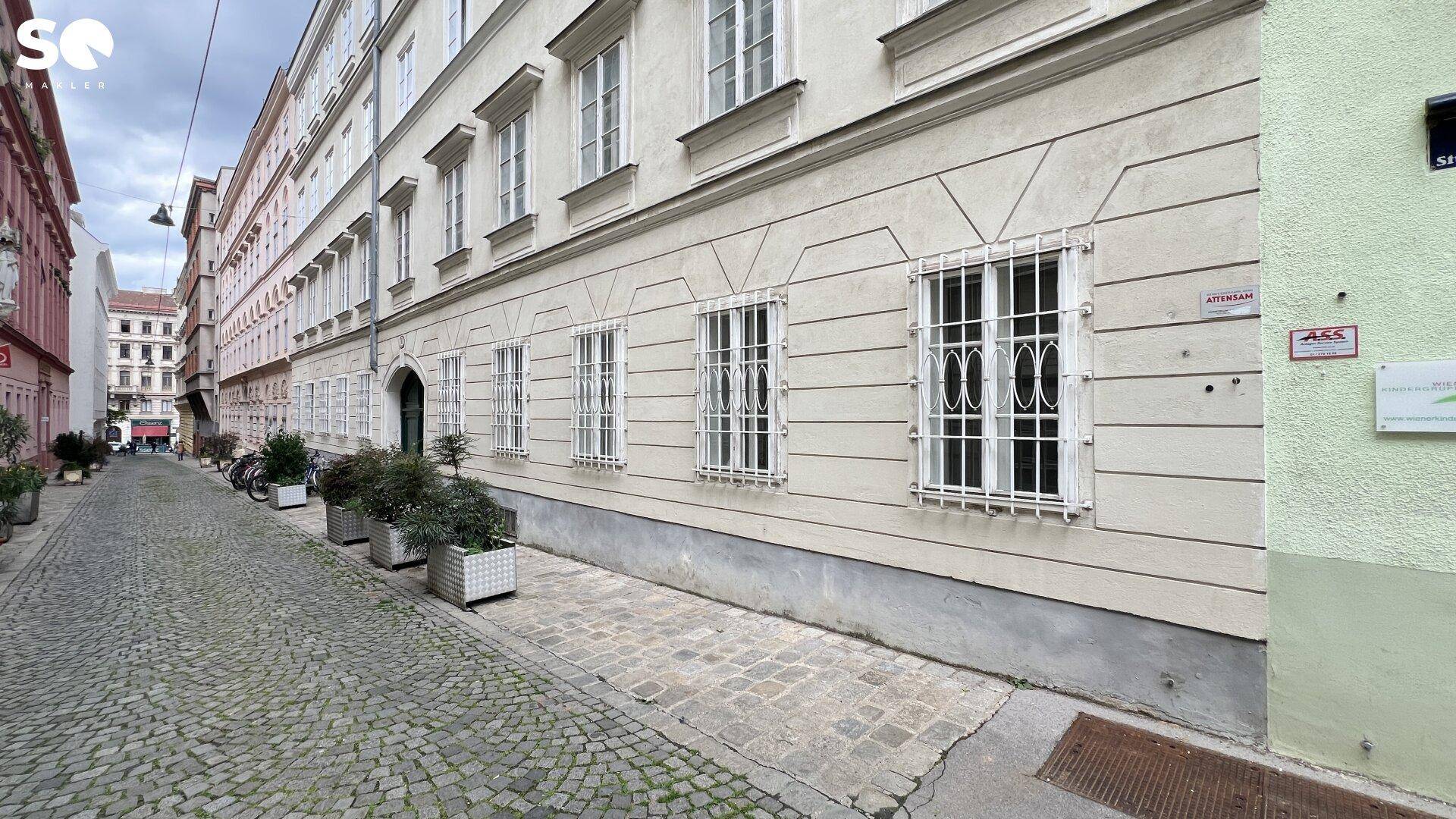 Ansicht der historischen Gebäudefassade von der gepflasterten Straße aus, umgeben von weiteren Häusern.
