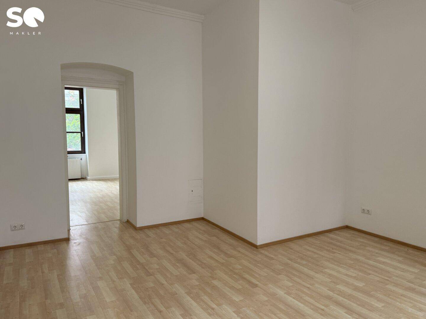 Helles, leeres Zimmer mit Holzboden und einem eleganten Rundbogen-Durchgang.