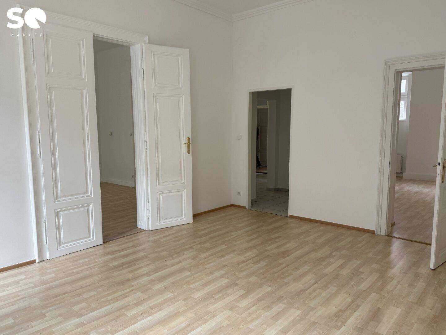 Großes, leeres Zimmer mit Holzboden und weit geöffneten Doppeltüren zu weiteren Räumen.