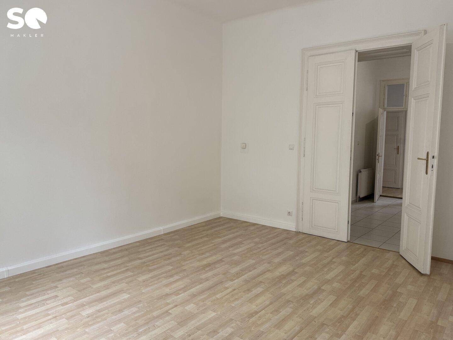 Leeres Zimmer mit Holzboden und Zugang zu einem Bereich mit Fliesenboden.