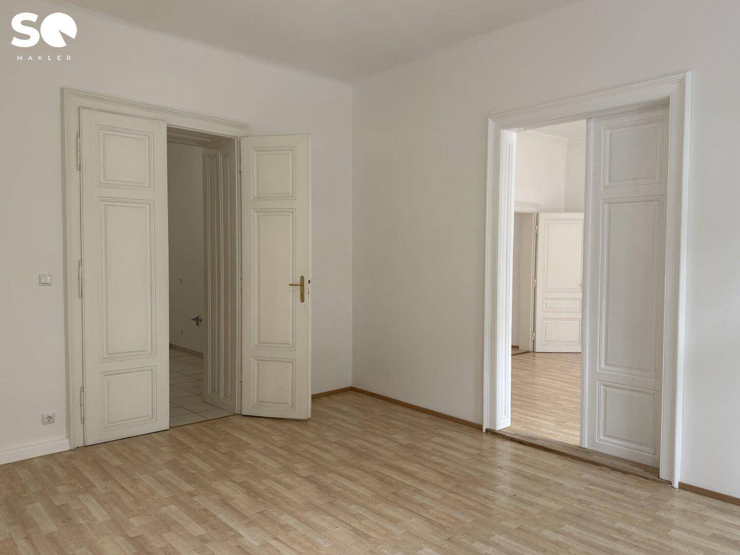 Helles Zimmer mit Holzboden und eleganten Doppeltüren, die zu weiteren Räumen führen.