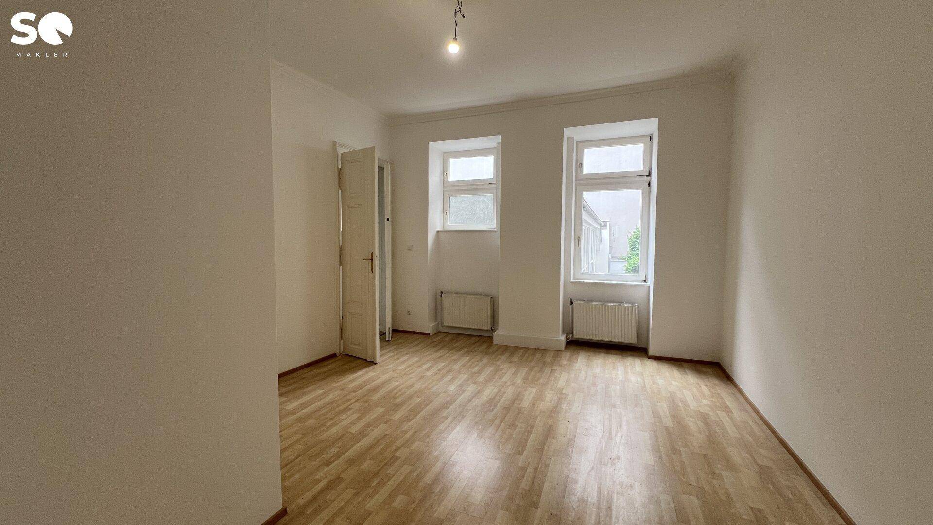 Helles, leeres Zimmer mit Holzboden und zwei Fenstern, ideal für Schlaf- oder Arbeitszimmer.