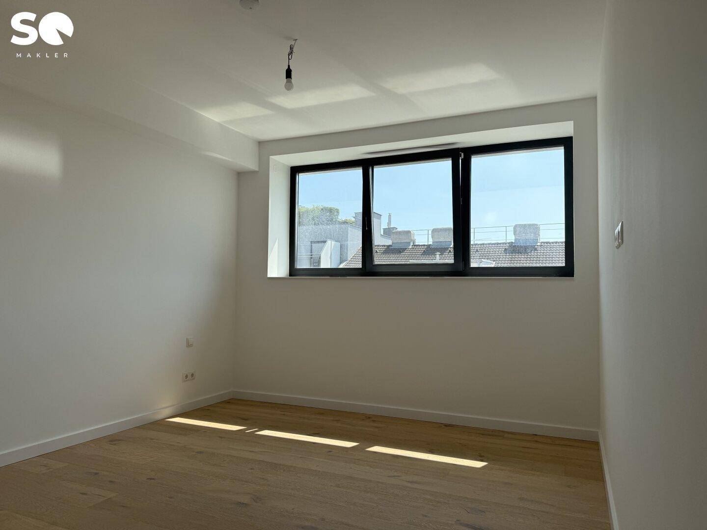 Helles Schlafzimmer mit Holzboden und einem Fenster, das einen Blick über die Dächer bietet.