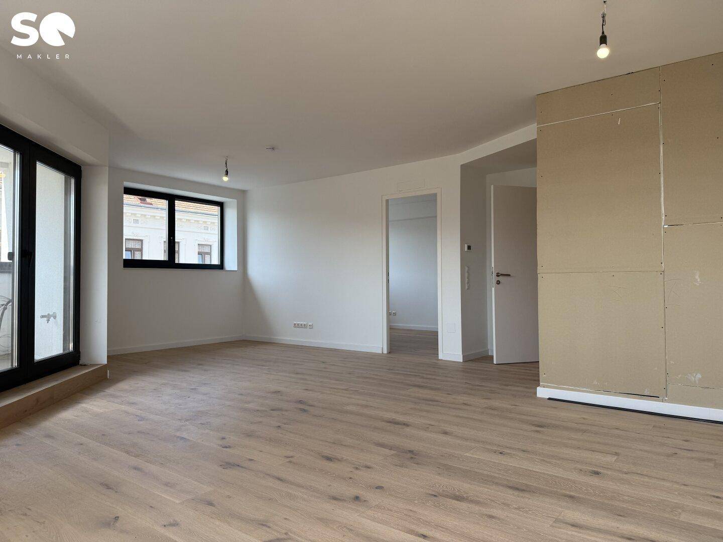 Großes, helles Wohnzimmer mit Holzboden, großen Fenstern und Zugang zu einem Außenbereich.