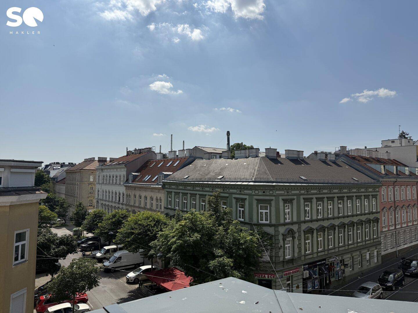 Weitblick von einem Balkon über eine grüne Allee und die Dächer der umliegenden Stadtgebäude.
