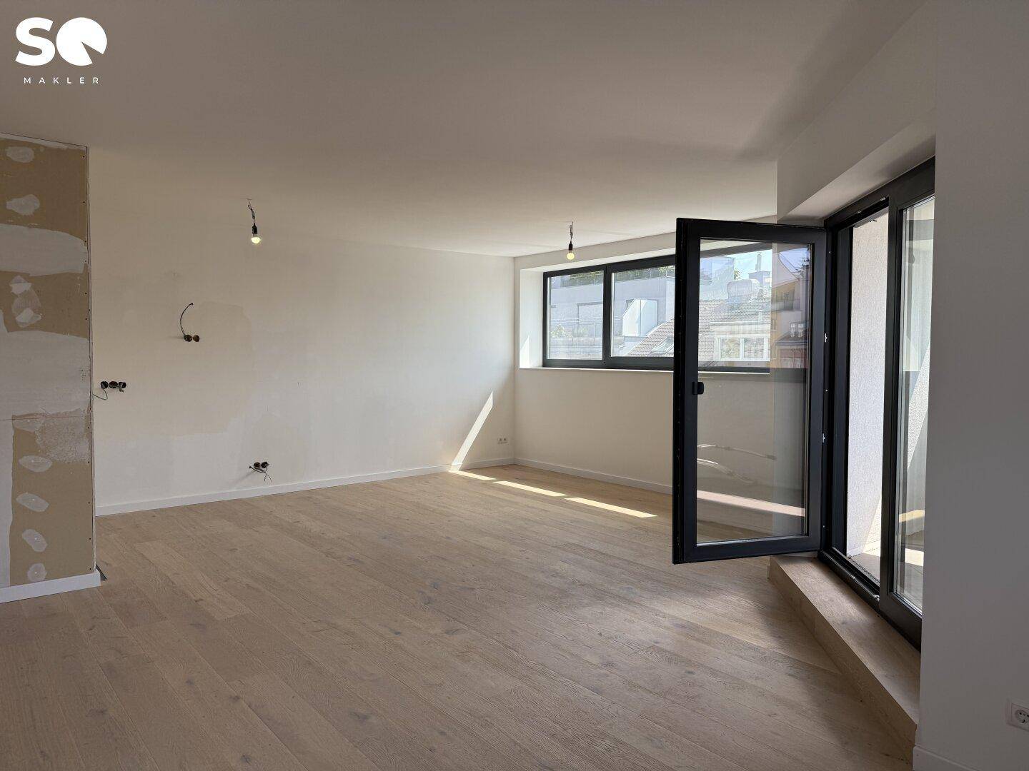 Helles Wohnzimmer mit neuem Holzboden, großen Fenstern und Zugang zu einem Außenbereich.