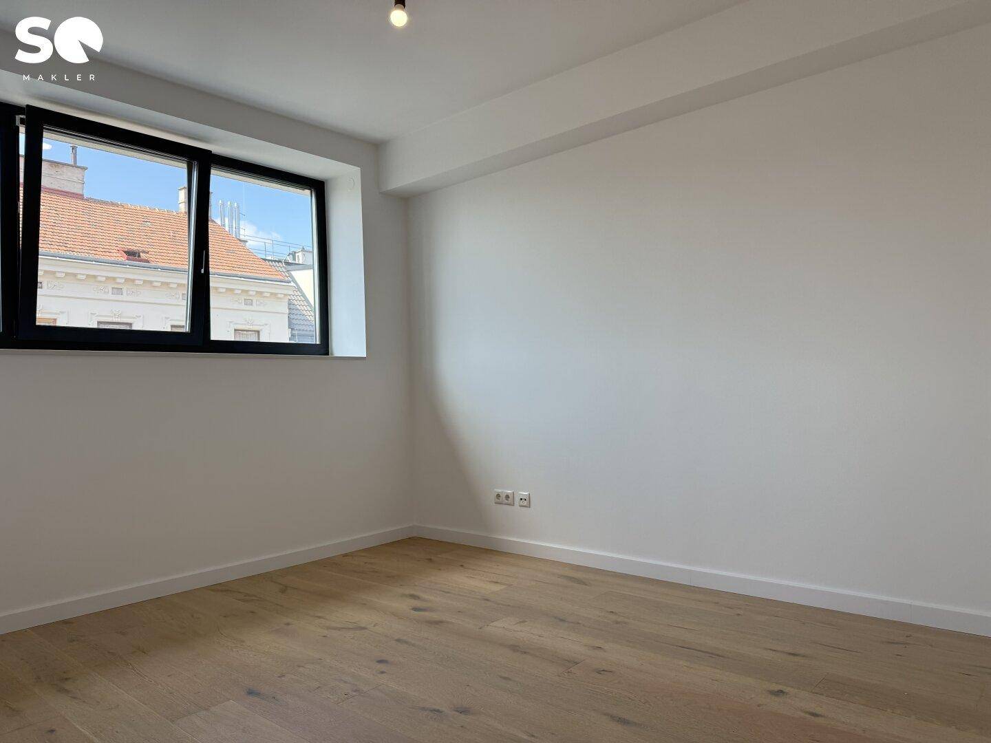 Helles Schlafzimmer mit Holzboden und einem Fenster, das einen weiten Blick über die Dächer bietet.