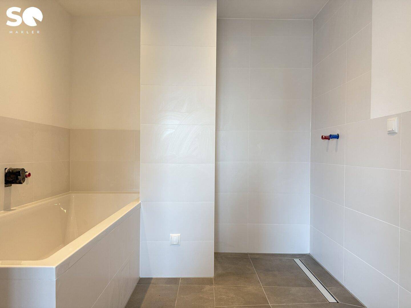 Modernes Badezimmer mit Badewanne und ebenerdiger Dusche, hell gefliesten Wänden und Boden.