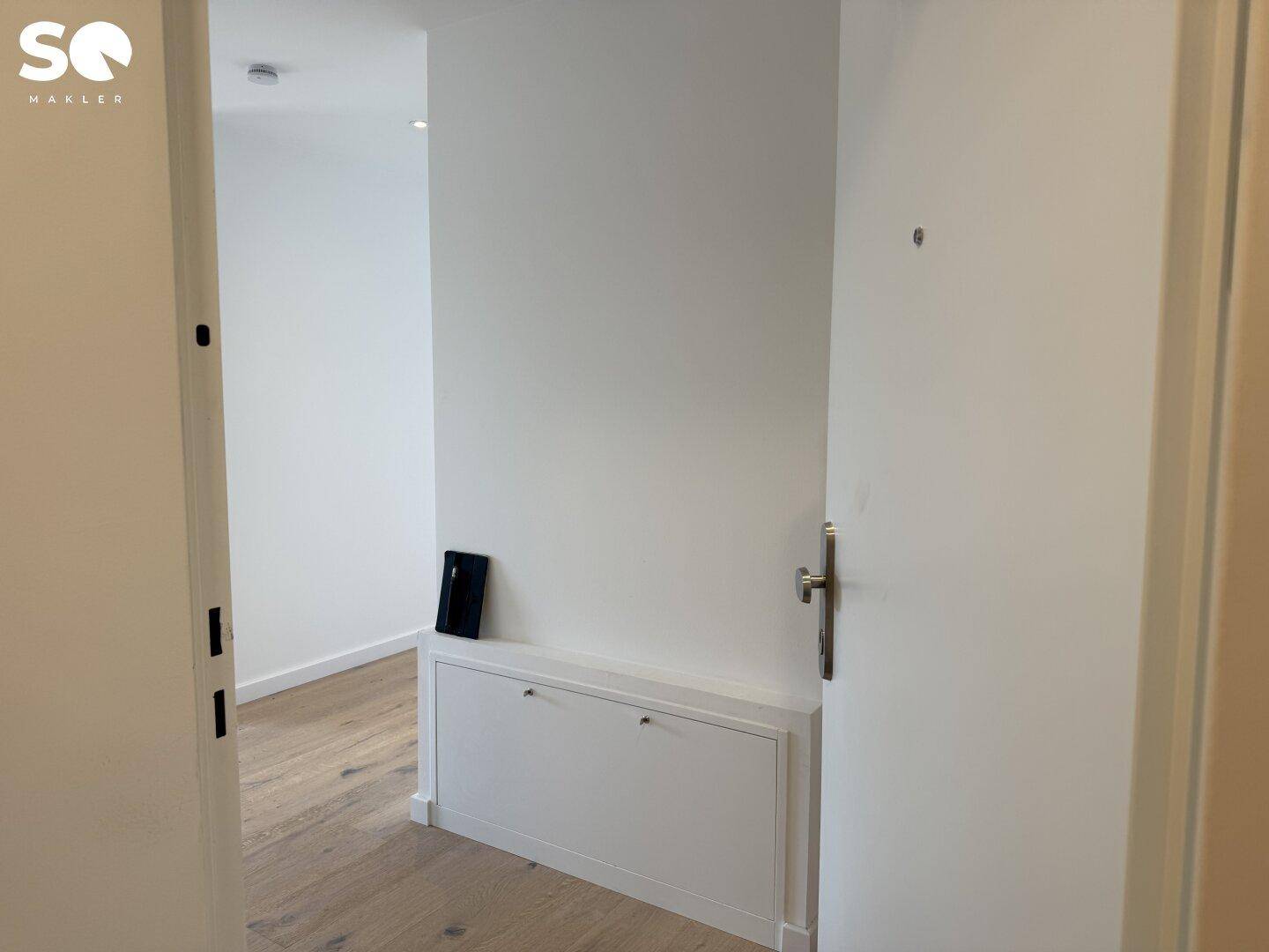 Eingangsbereich mit hellem Holzboden, weißer Tür und einem praktischen Einbauschrank.