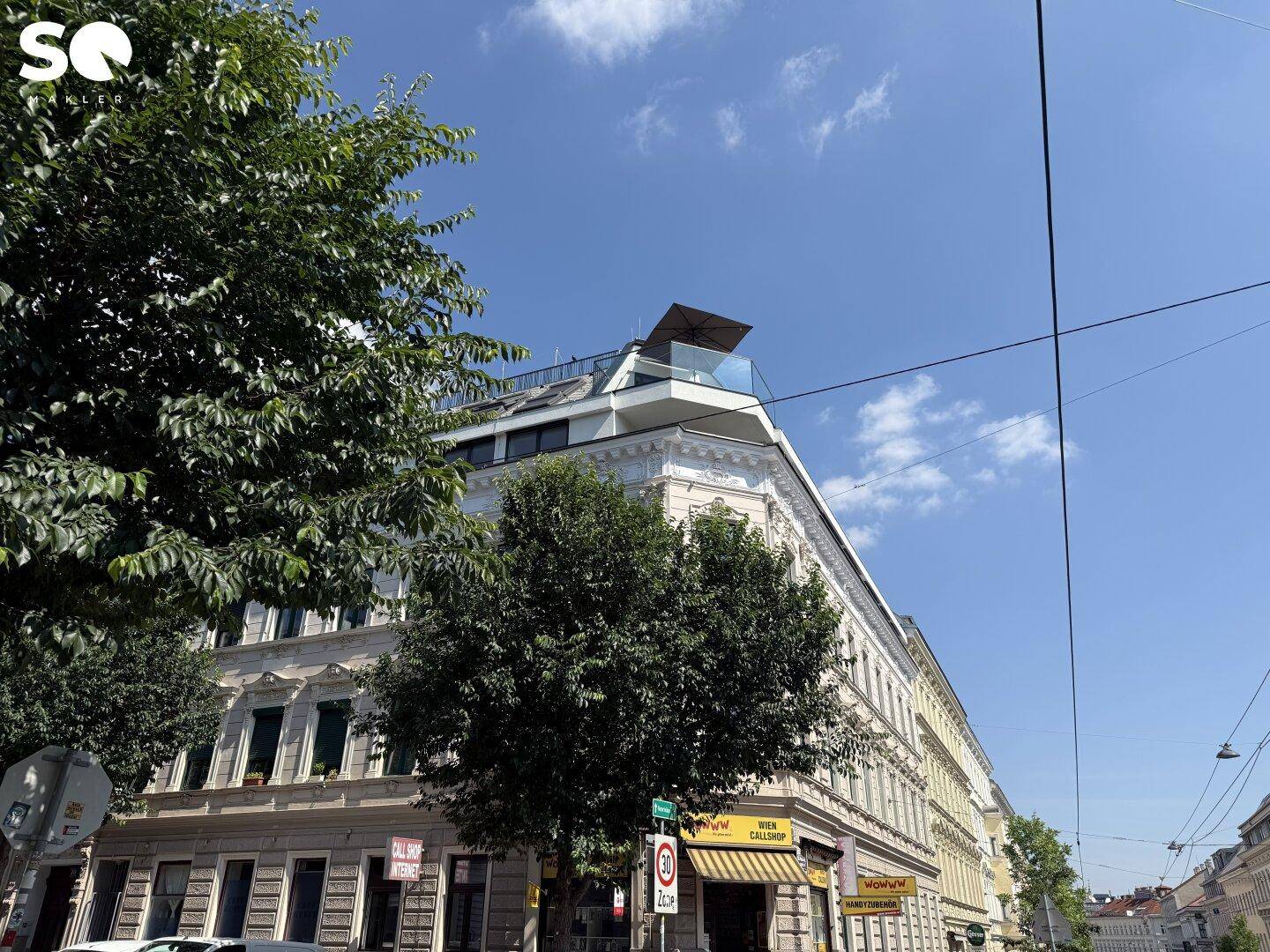 Weitwinkelaufnahme des Eckgebäudes mit historischer Fassade, modernem Dachausbau und klarem Himmel.