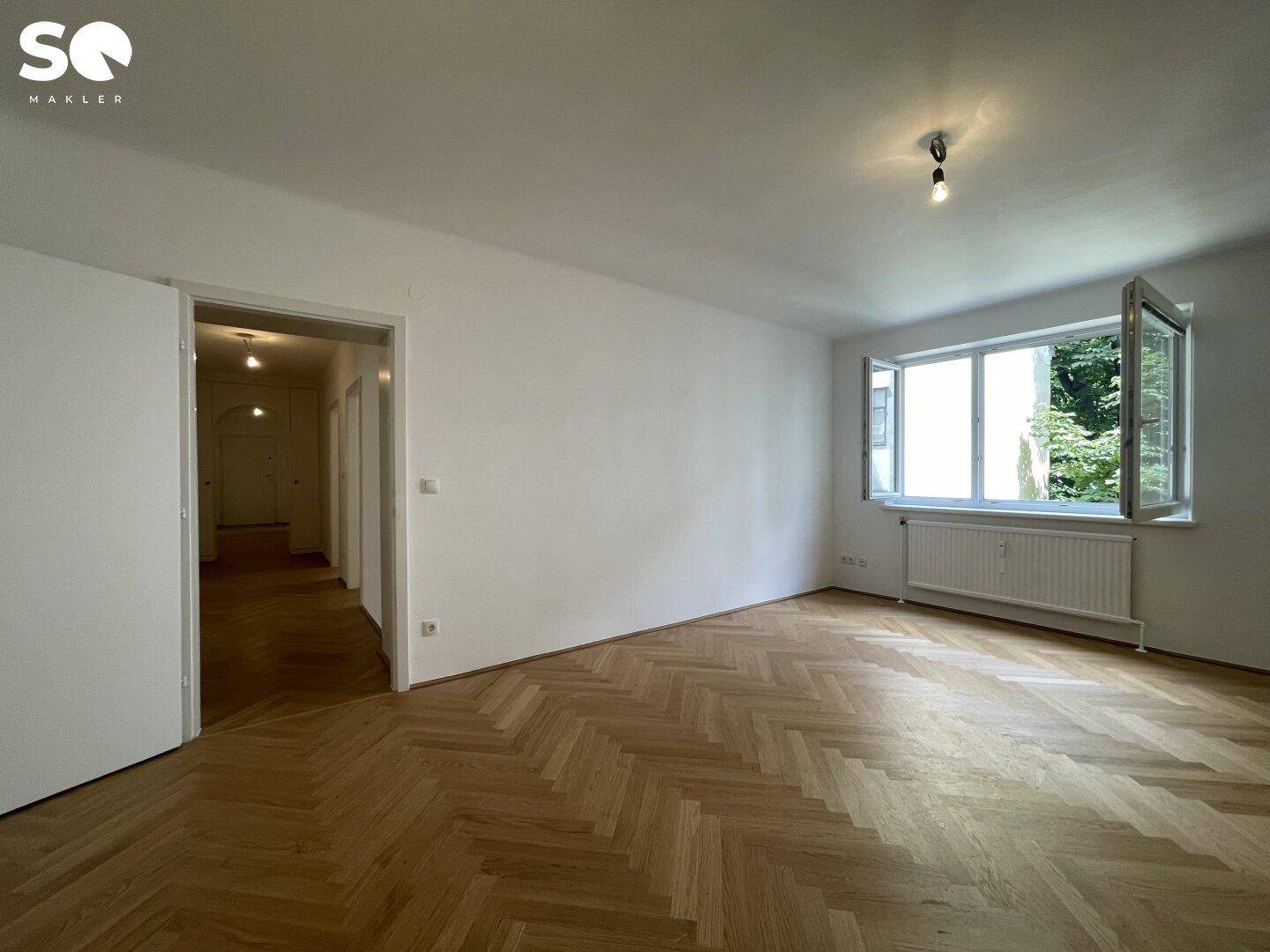 Helles Zimmer mit Fischgrätparkett und Zugang zum Flur, mit Blick ins Grüne.