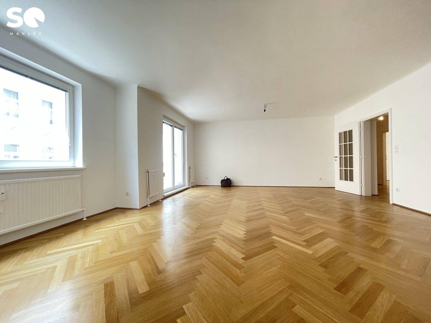 Geräumiges Wohnzimmer mit Fischgrätparkett und Zugang zu weiteren Räumen.