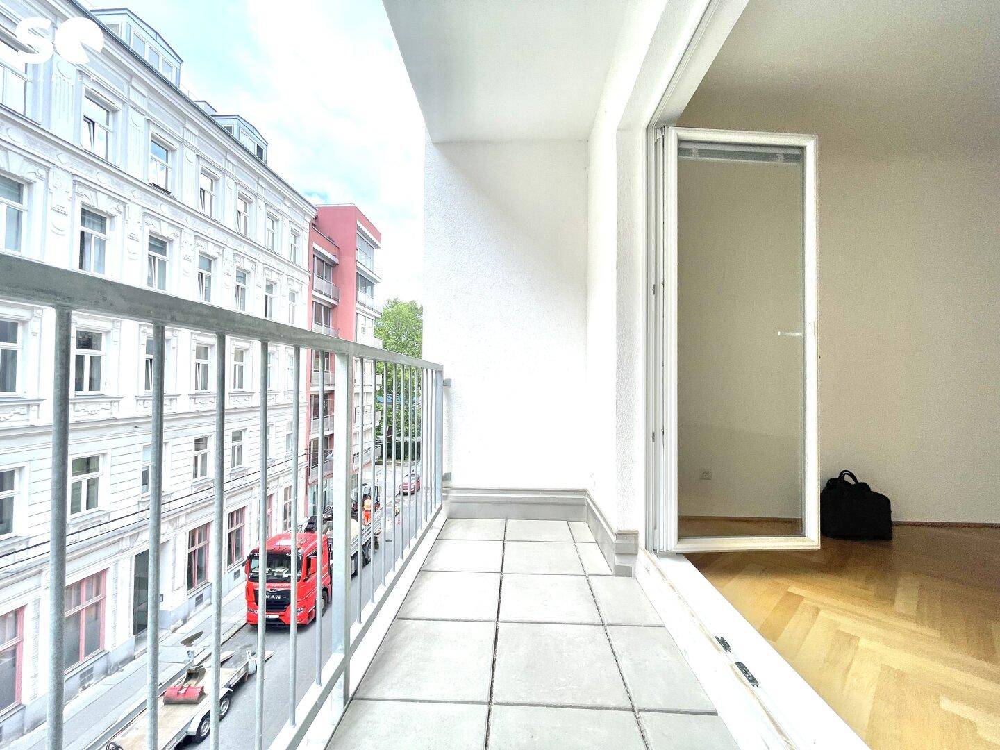 Langer Balkon mit Fliesenboden und Blick auf die angrenzenden Gebäude und die Straße.