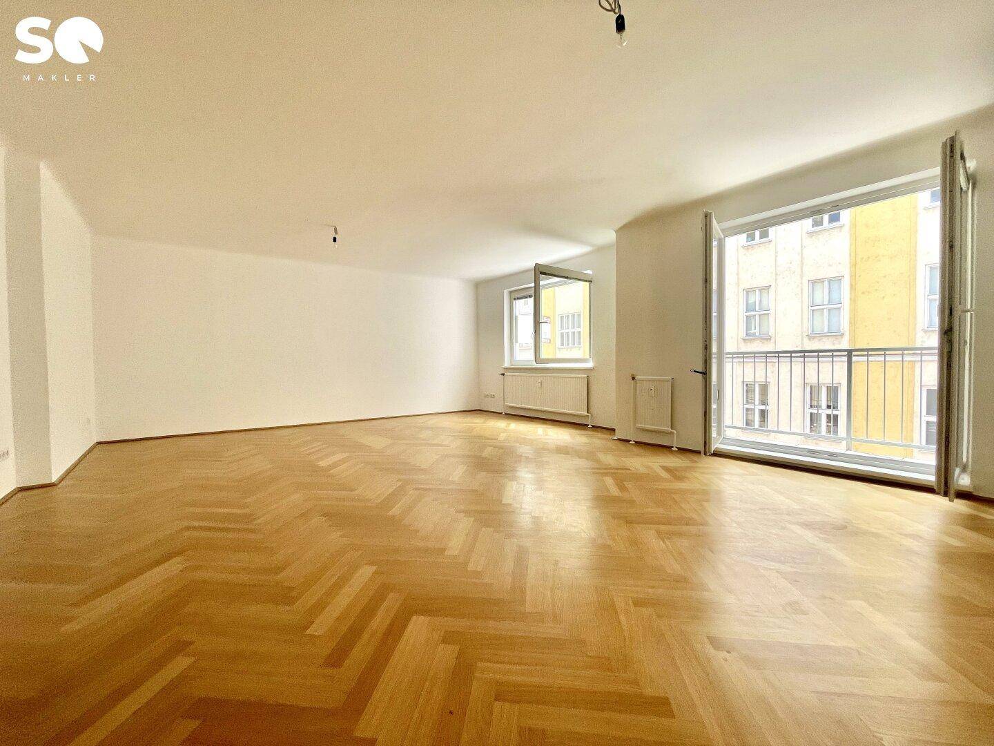 Großzügiges, leeres Wohnzimmer mit klassischem Fischgrätparkett und viel Tageslicht.