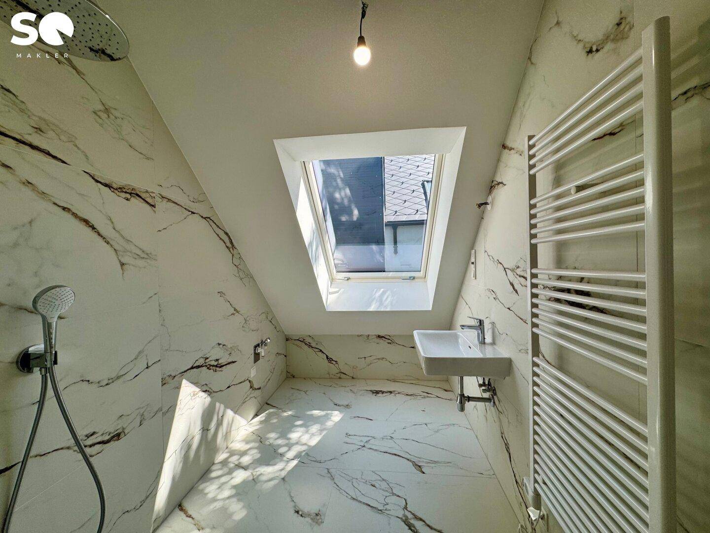 Helles Badezimmer im Dachgeschoss mit Marmorfliesen, Dachfenster und moderner Duscharmatur.