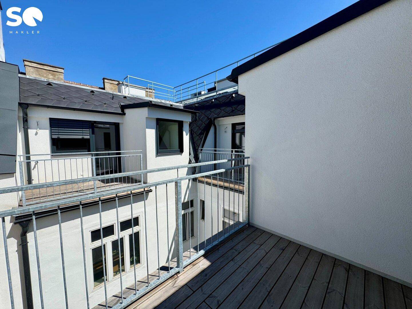 Balkon mit Holzboden und Blick auf die umliegenden Gebäude und weitere Balkone.
