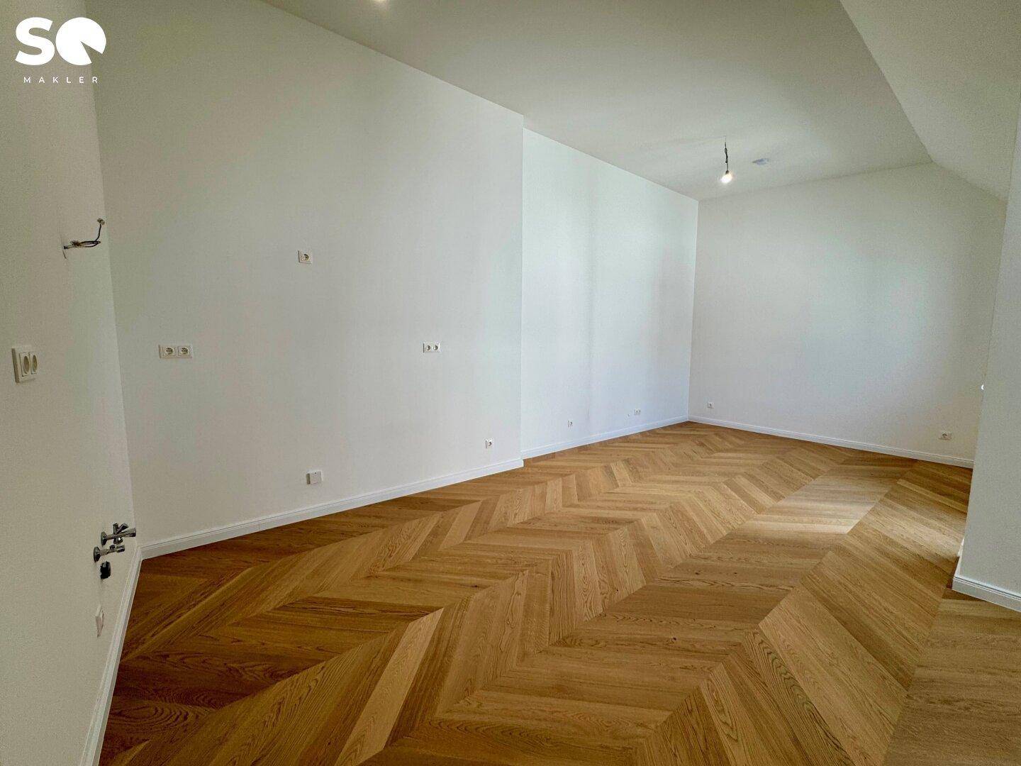 Helles und geräumiges Zimmer im Dachgeschoss mit hochwertigem Fischgrätparkett und weißen Wänden.