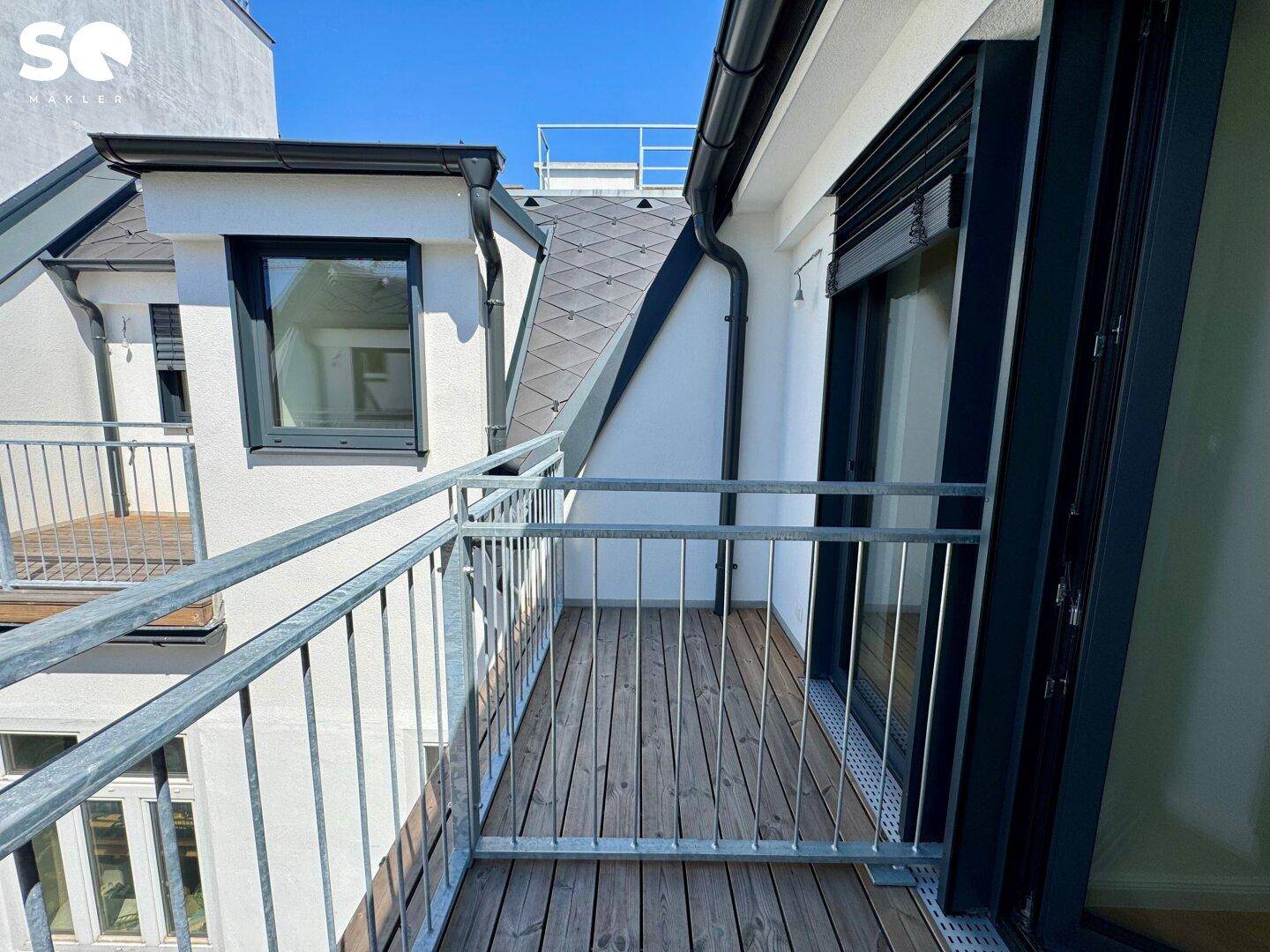 Schmaler Balkon mit Holzboden und Metallgeländer, bietet einen Blick auf die Gebäudestruktur.