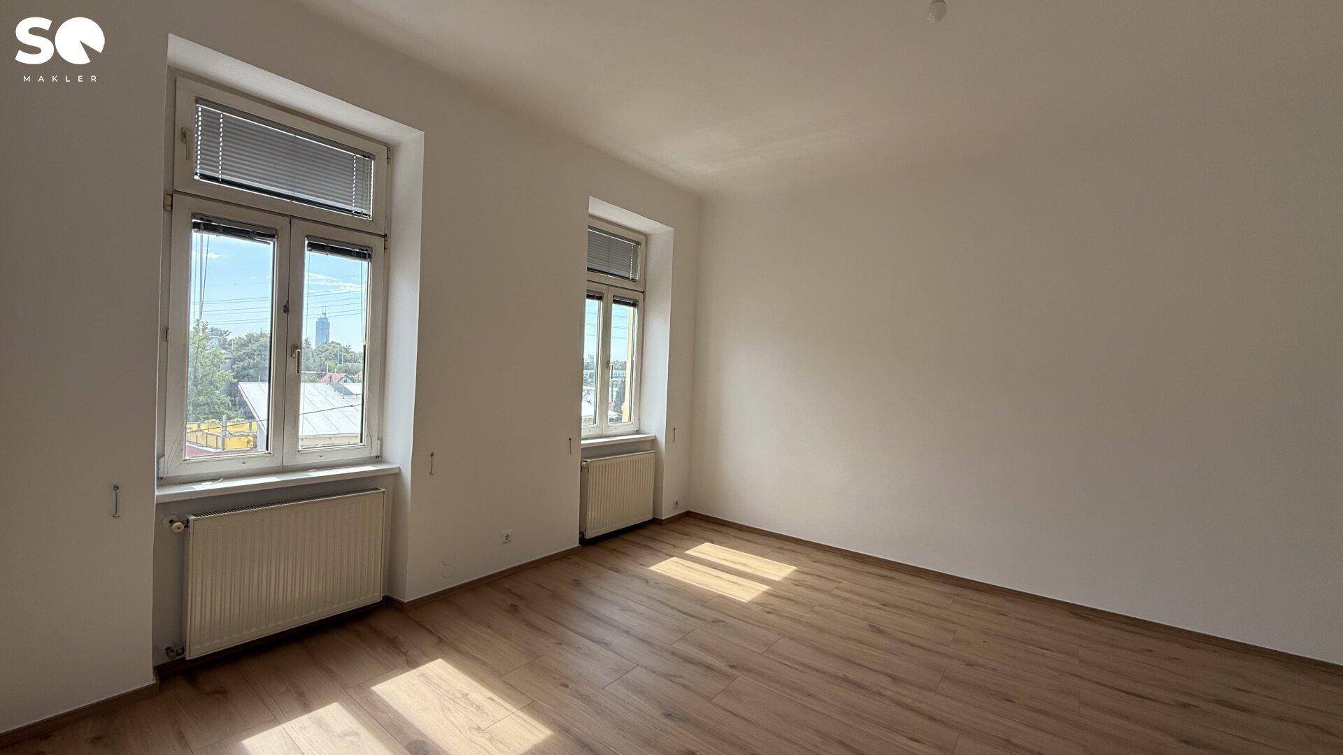 Geräumiges, helles Zimmer mit Holzboden und zwei Fenstern, ideal für Wohn- oder Schlafbereich.