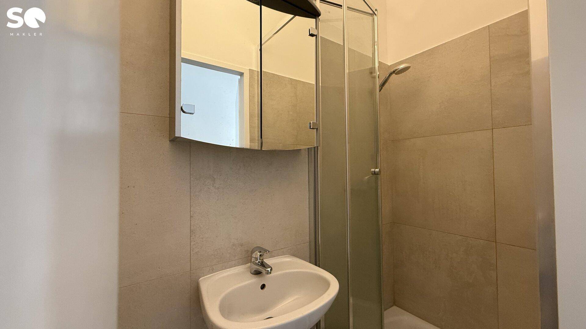 Modernes Badezimmer mit Waschbecken, Spiegelschrank und Duschkabine, hell gefliest.