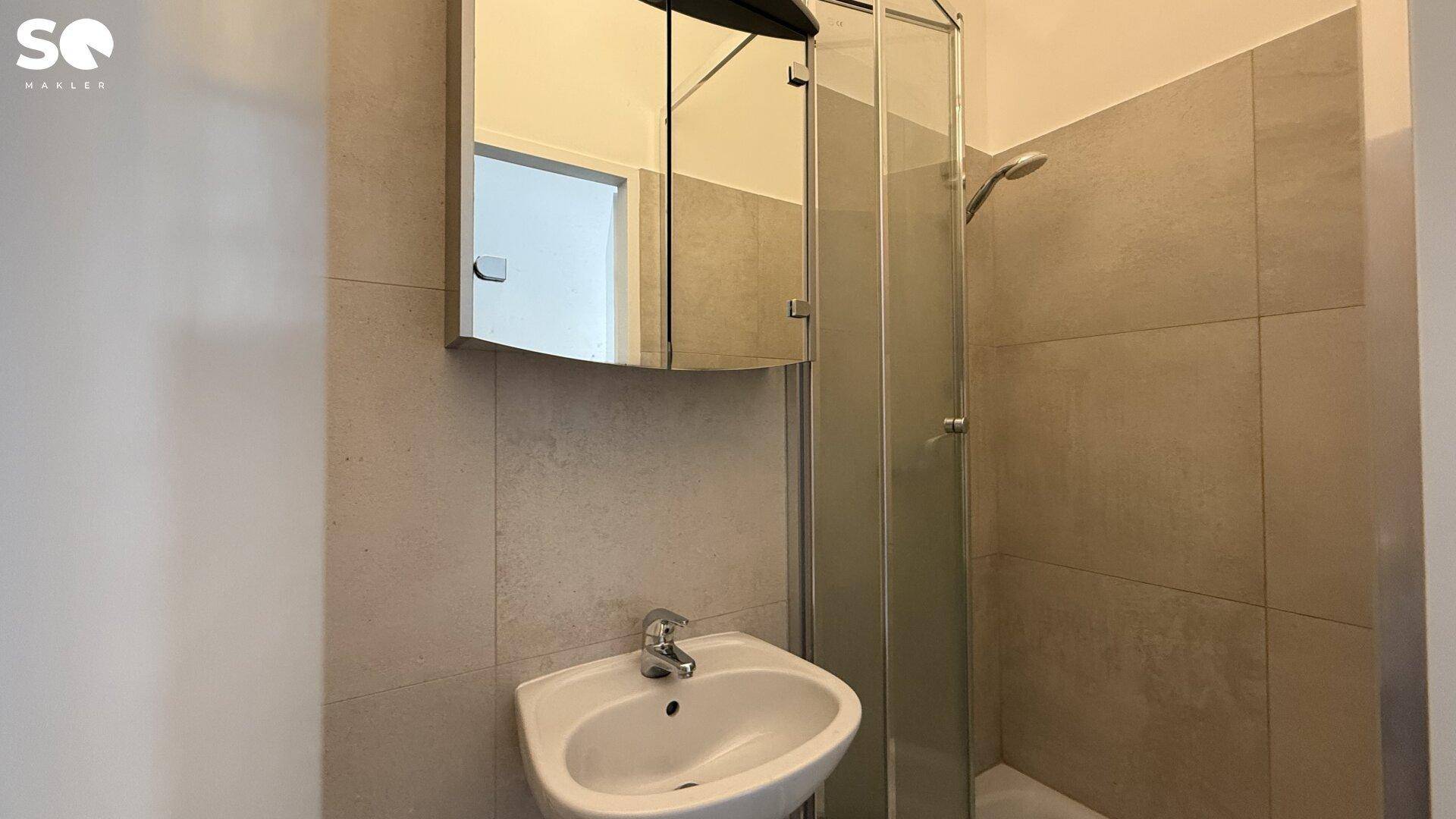 Funktionales Badezimmer mit Duschkabine, Waschbecken und Spiegelschrank, in neutralen Farben.