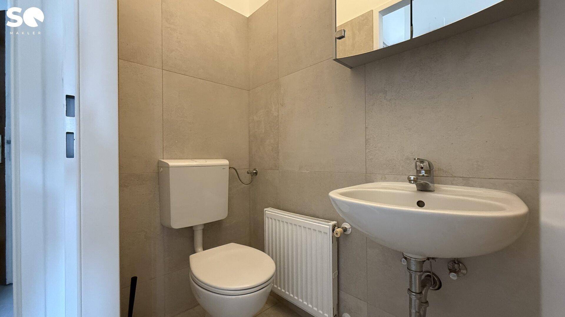 Kleines WC mit Toilette, Waschbecken und Heizkörper, komplett gefliest.
