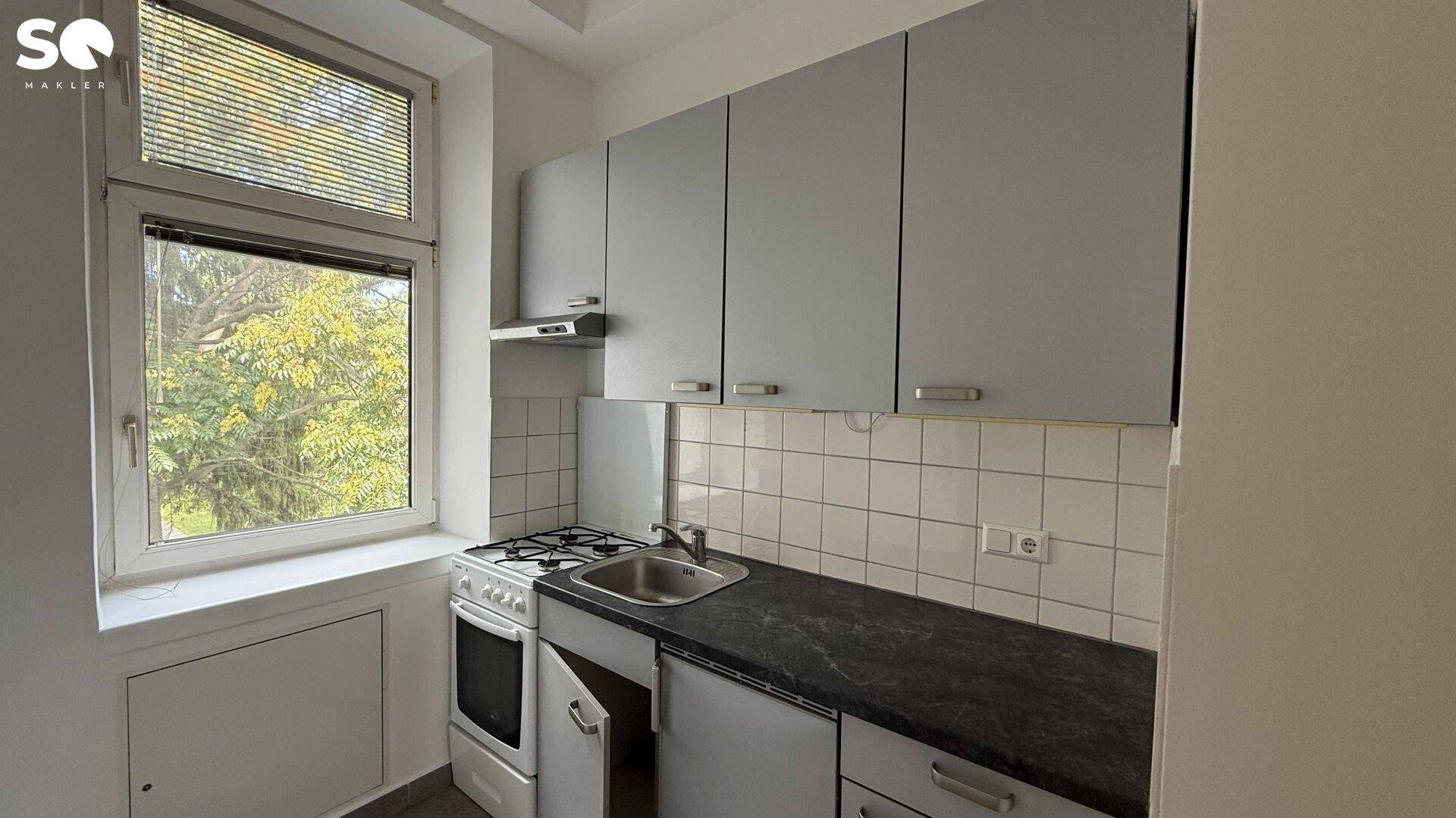 Funktionale Küche mit grauen Oberschränken, Gasherd und Fenster mit Blick ins Grüne.