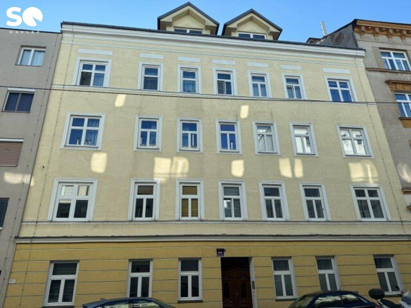 Klassische Fassade eines Mehrfamilienhauses in hellem Gelb mit vielen Fenstern und Dachgauben, typisch für einen Altbau.