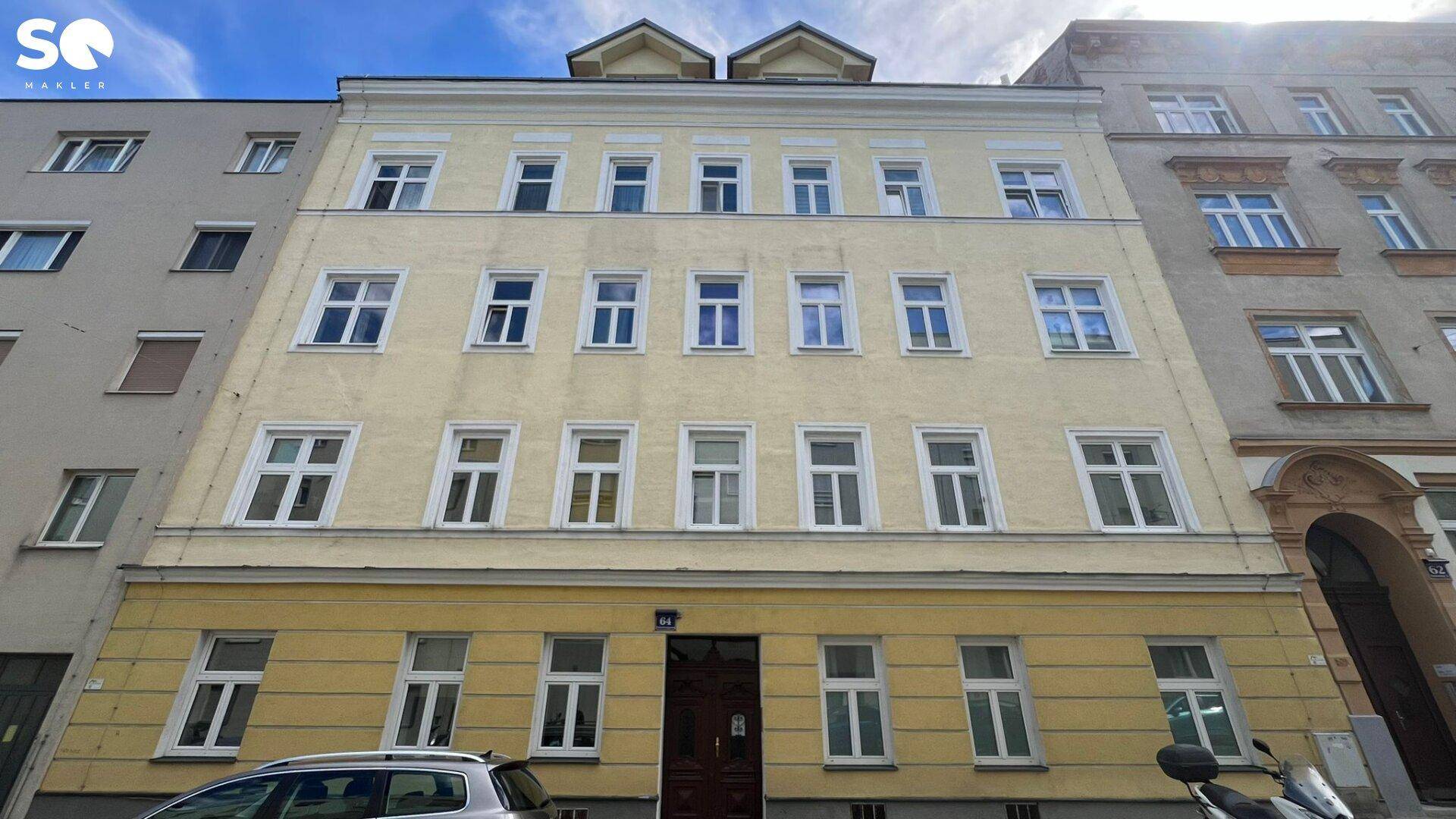 Klassische Fassade eines Mehrfamilienhauses in hellem Gelb mit vielen Fenstern und Dachgauben, typisch für einen Altbau.