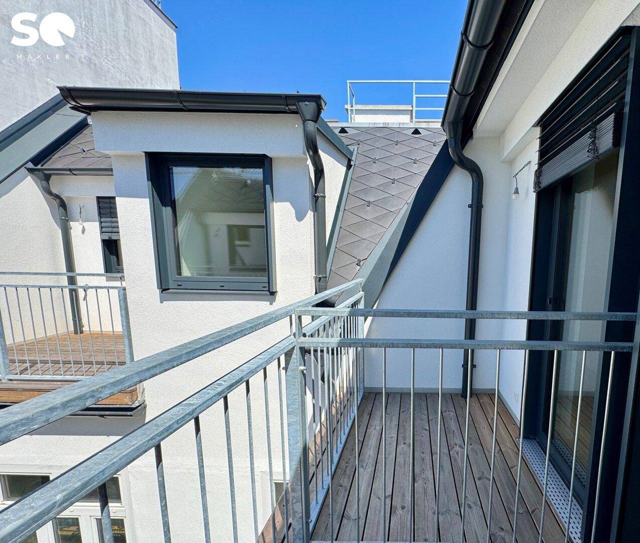 Kleiner Balkon mit Holzboden und Metallgeländer, der einen Blick auf die umliegenden Gebäude bietet.
