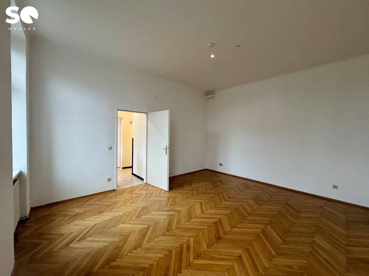 Geräumiges Zimmer mit klassischem Fischgrätparkett und weiß gestrichenen Wänden.