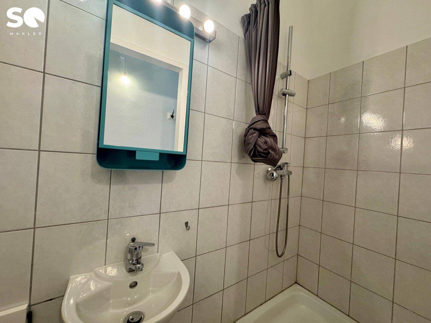 Kleines Badezimmer mit weißen Fliesen, Waschbecken und Duschbereich mit Vorhang.