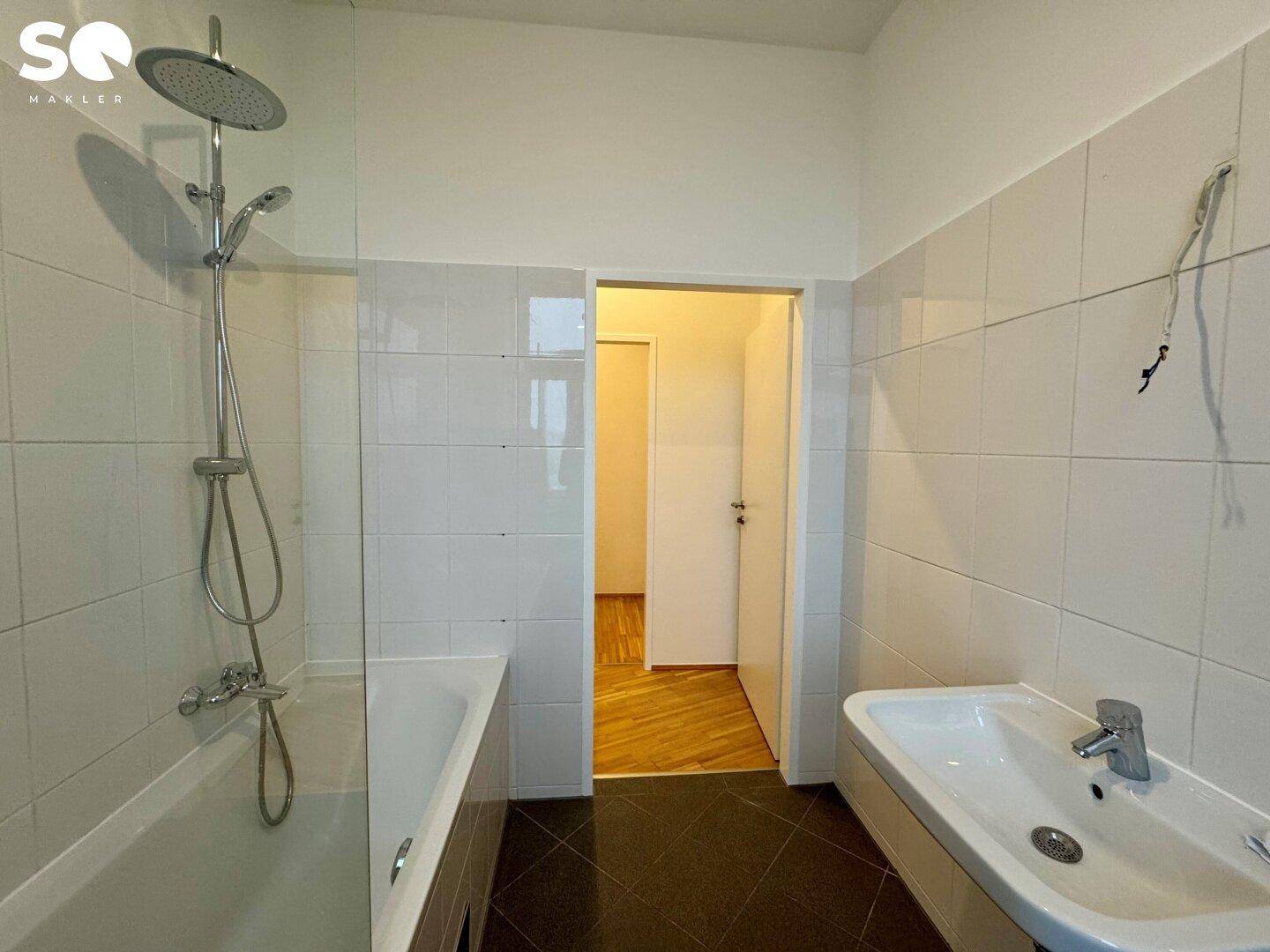 Badezimmer mit Badewanne, Duscharmatur, Waschbecken und weißen Fliesen an den Wänden.