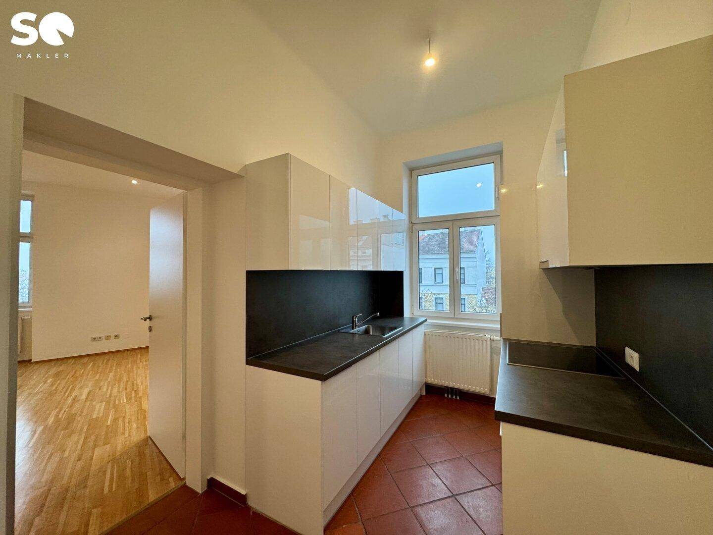 Moderne Küche mit weißen Hochglanzschränken, dunkler Arbeitsplatte und Terrakotta-Fliesenboden.