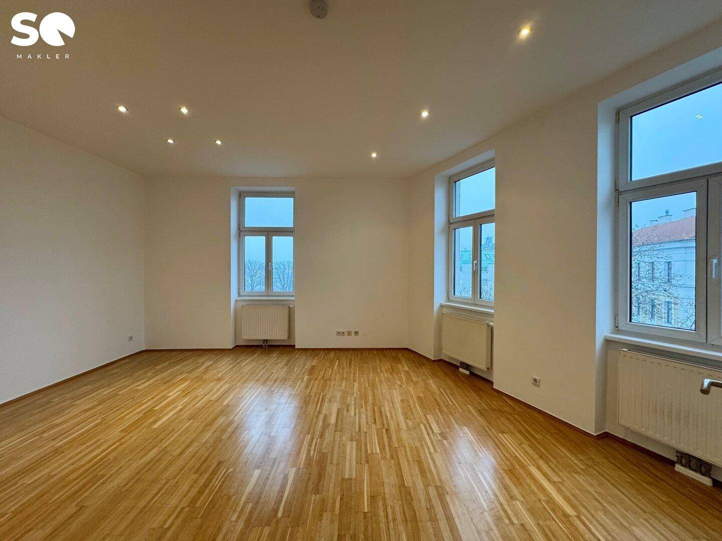 Geräumiges Wohnzimmer mit Parkettboden, Einbaustrahlern und mehreren Fenstern mit Stadtblick.