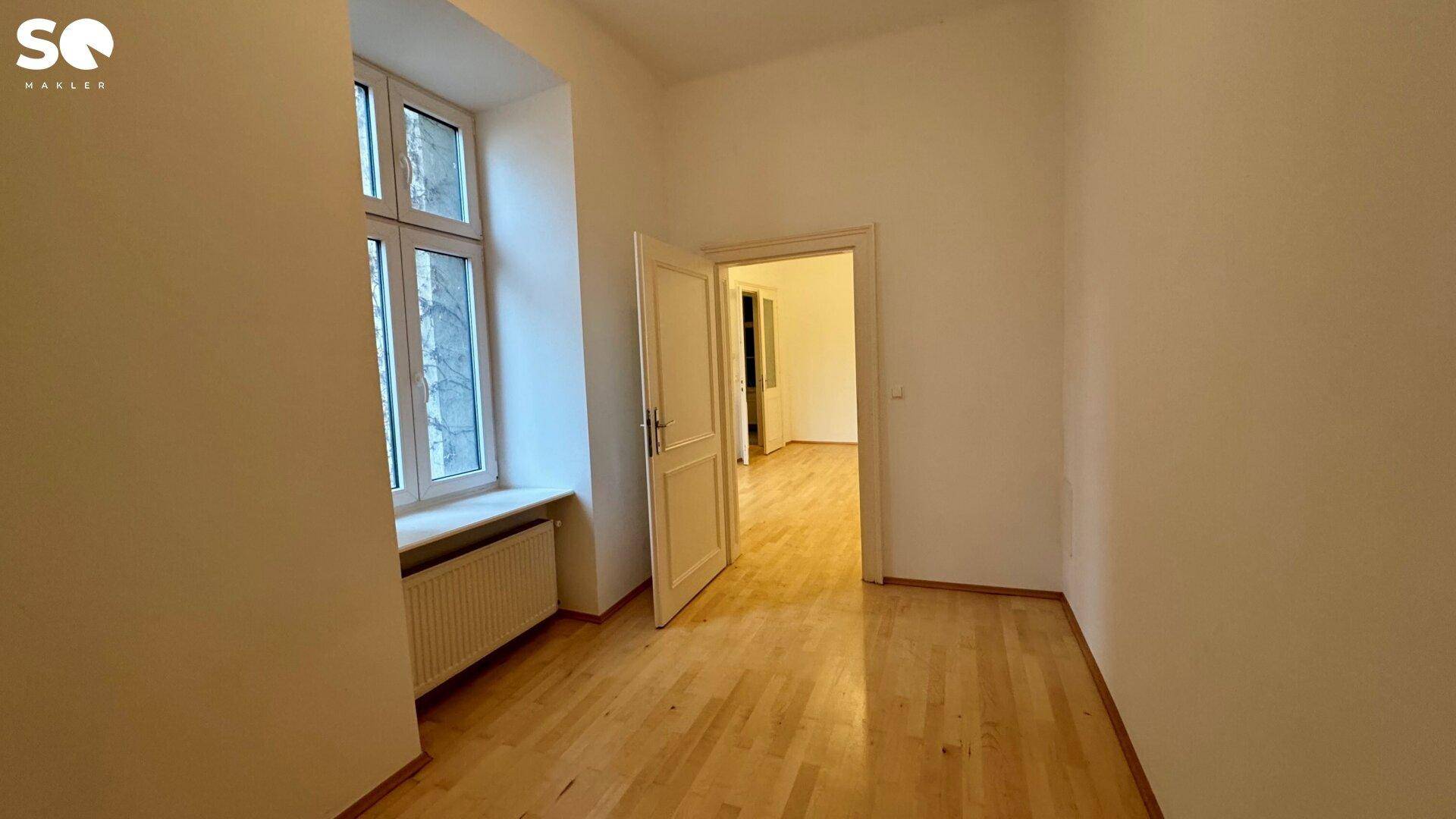 Unmöbliertes Zimmer mit Holzboden und Fenster, das einen Blick nach draußen bietet.