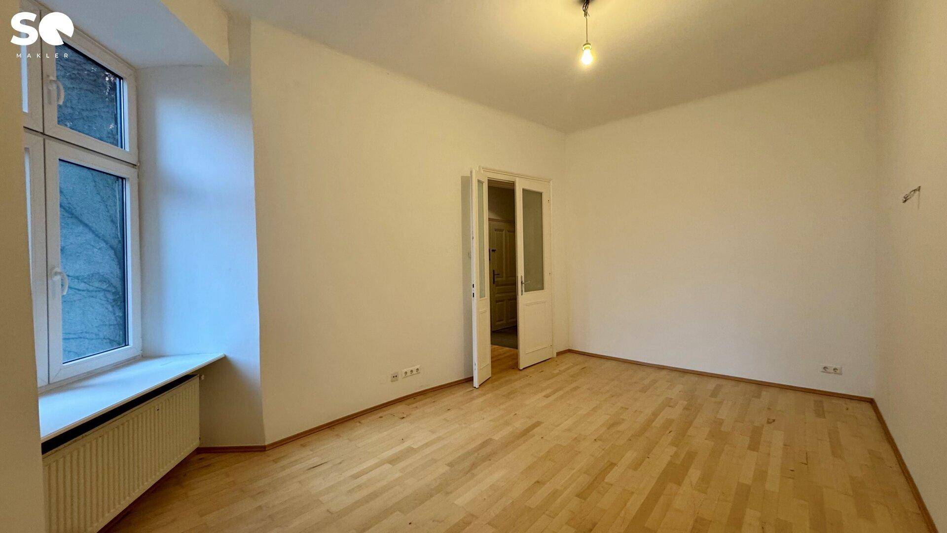 Helles, unmöbliertes Zimmer mit Parkettboden und großem Fenster, das viel Tageslicht hereinlässt.