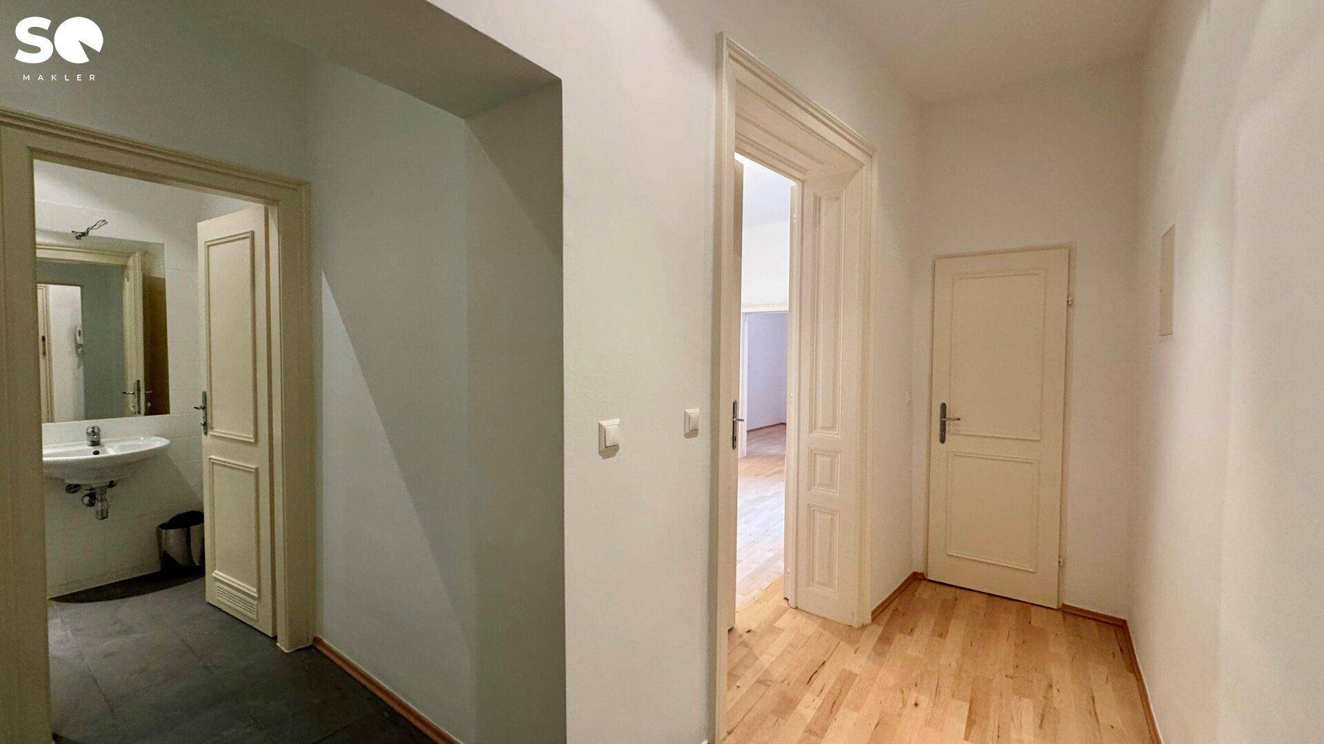Heller Flur mit Parkettboden, der zu einem Badezimmer mit Waschbecken führt.