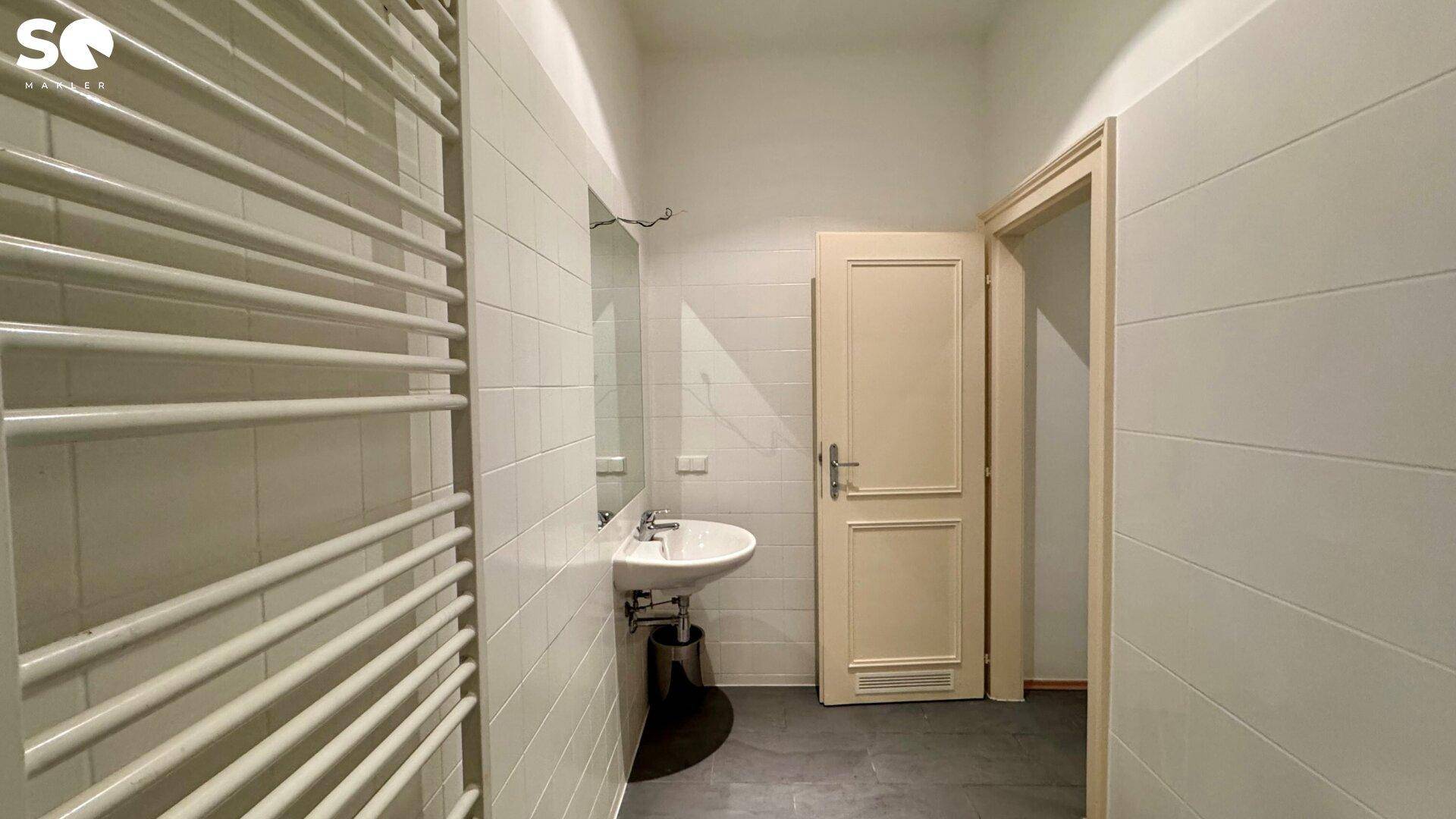 Funktionales Badezimmer mit Waschbecken, Spiegel und Handtuchheizkörper, gefliest in Weiß.