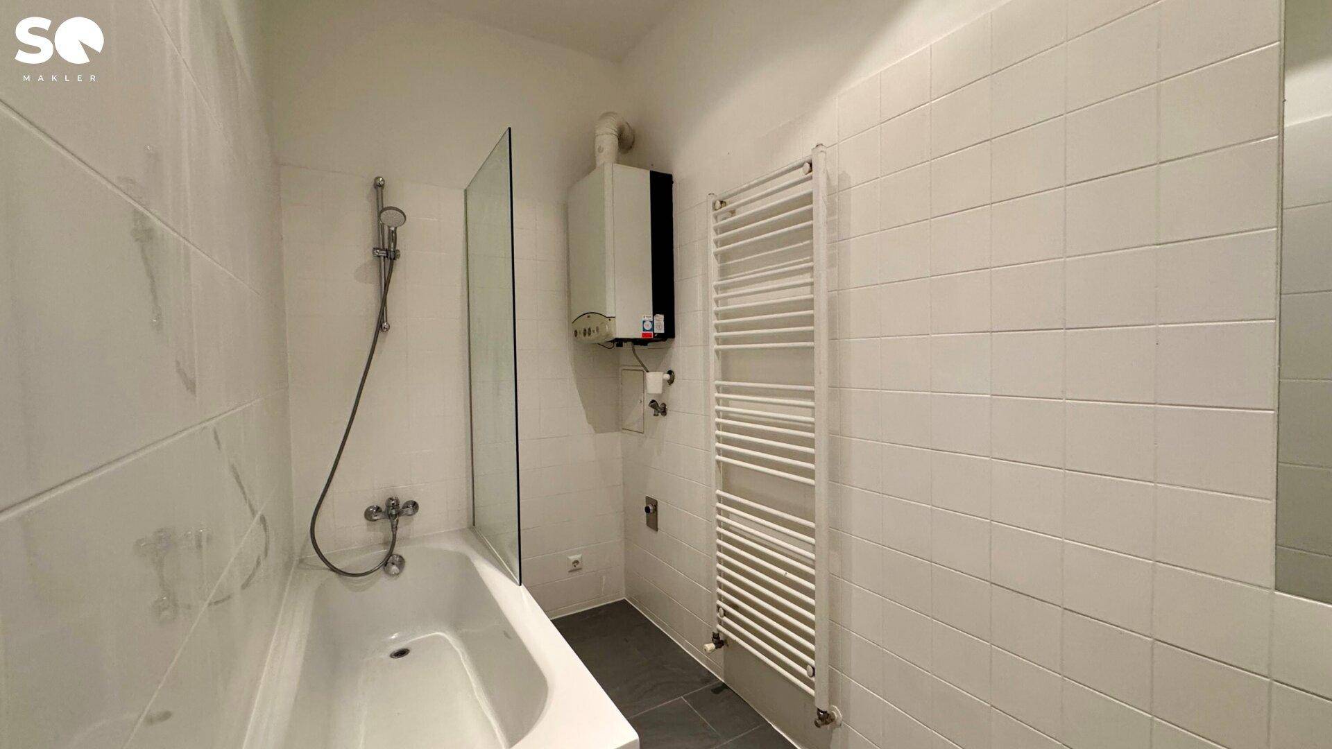 Helles Badezimmer mit Badewanne, Duscharmatur, Handtuchheizkörper und Gastherme.