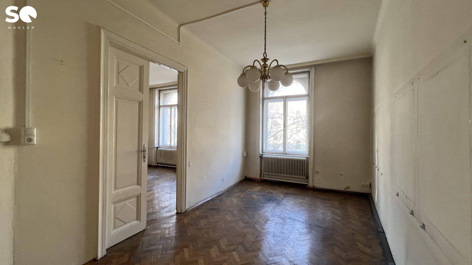 Helles Zimmer mit Fischgrätparkett und Kronleuchter, das auf eine Modernisierung wartet.