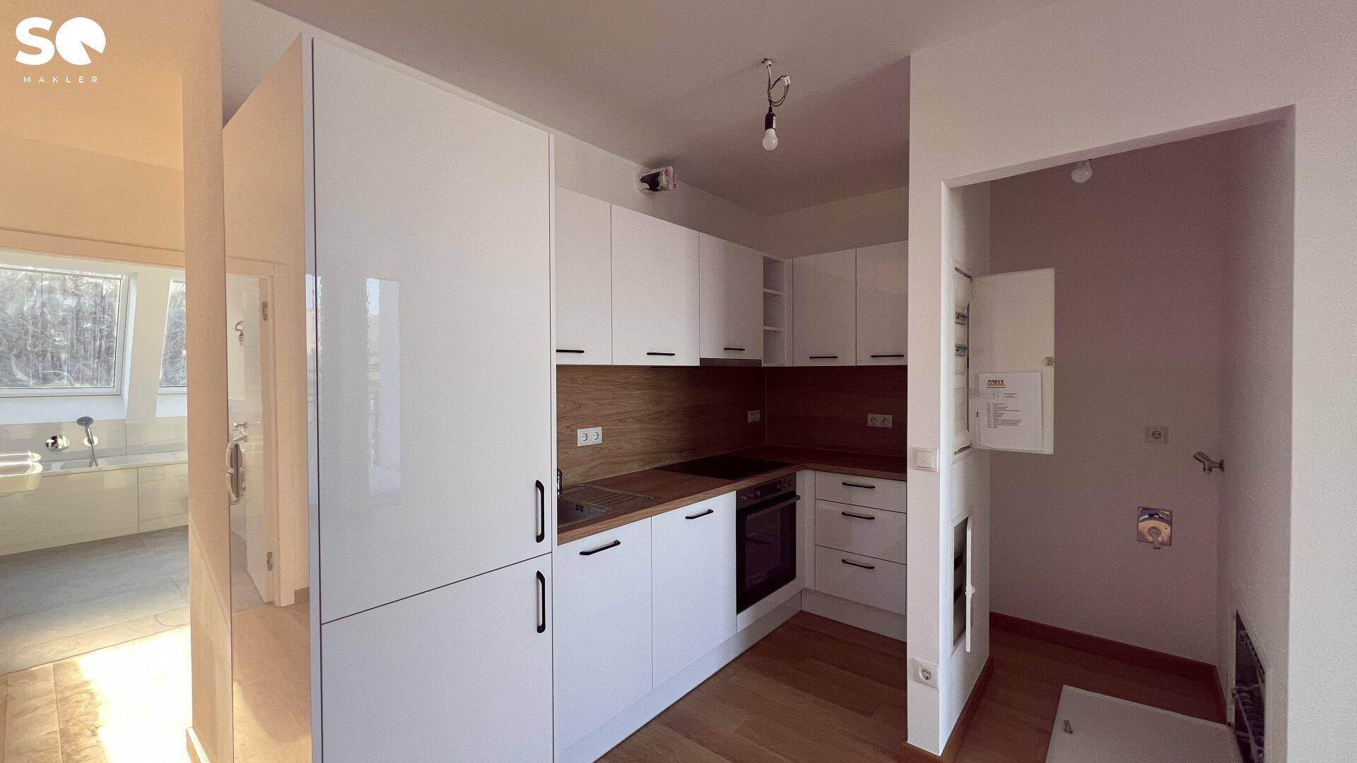Moderne weiße Küche mit Holzarbeitsplatten, integrierten Geräten und Blick in ein angrenzendes Badezimmer.