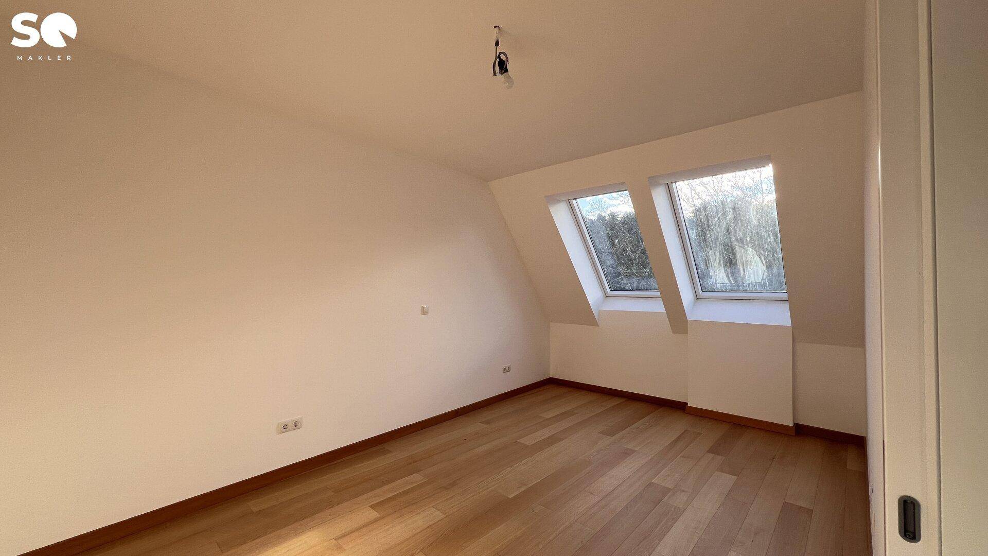 Ruhiges Schlafzimmer mit Holzboden, weißen Wänden und zwei Dachfenstern, die viel Tageslicht hereinlassen.