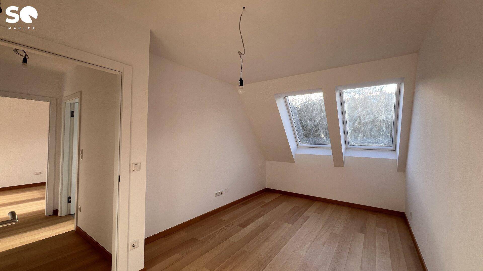 Helles Zimmer mit Holzboden und Dachschrägen, ausgestattet mit zwei Dachfenstern für optimale Belichtung.