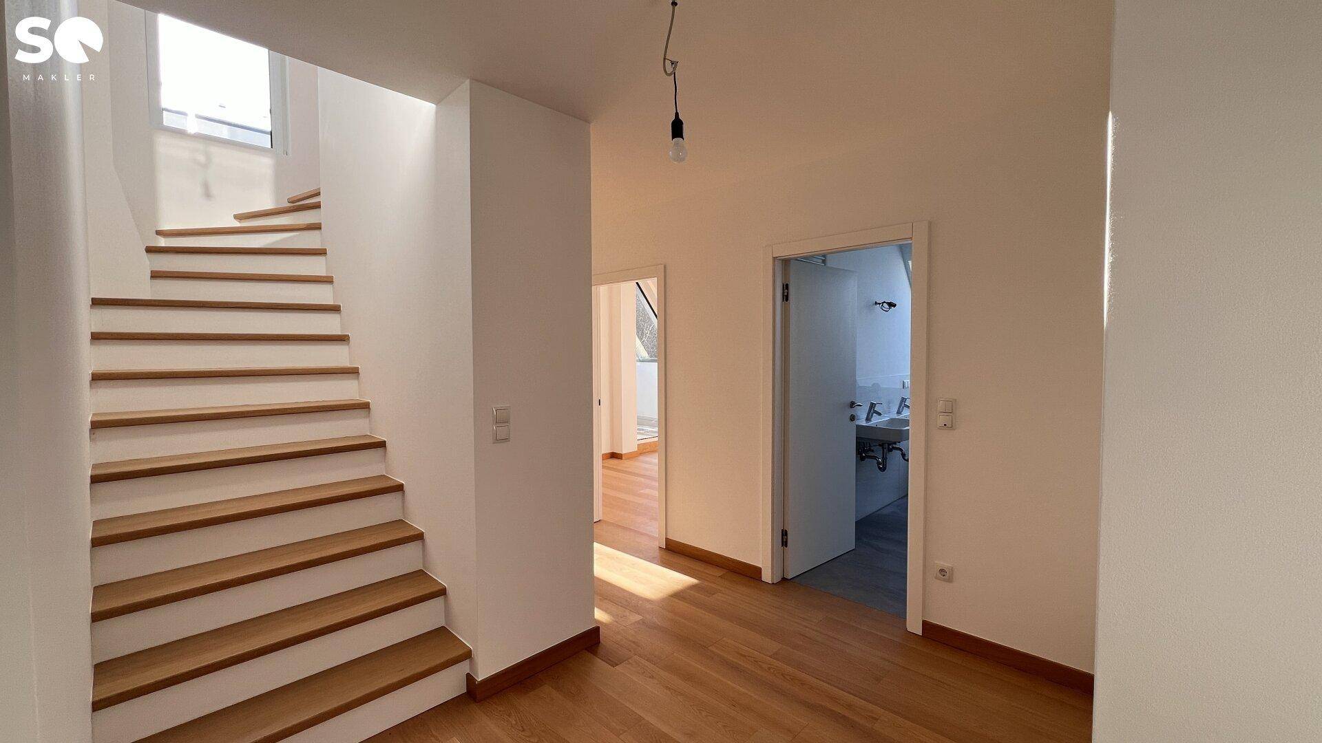 Heller Flur mit Holztreppe und Zugang zu weiteren Räumen, inklusive Badezimmer.