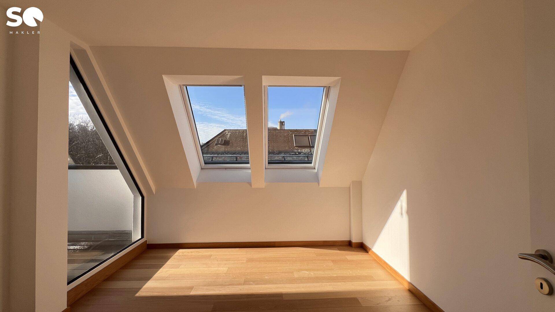 Helles Zimmer im Dachgeschoss mit Holzboden und zwei großen Dachfenstern.