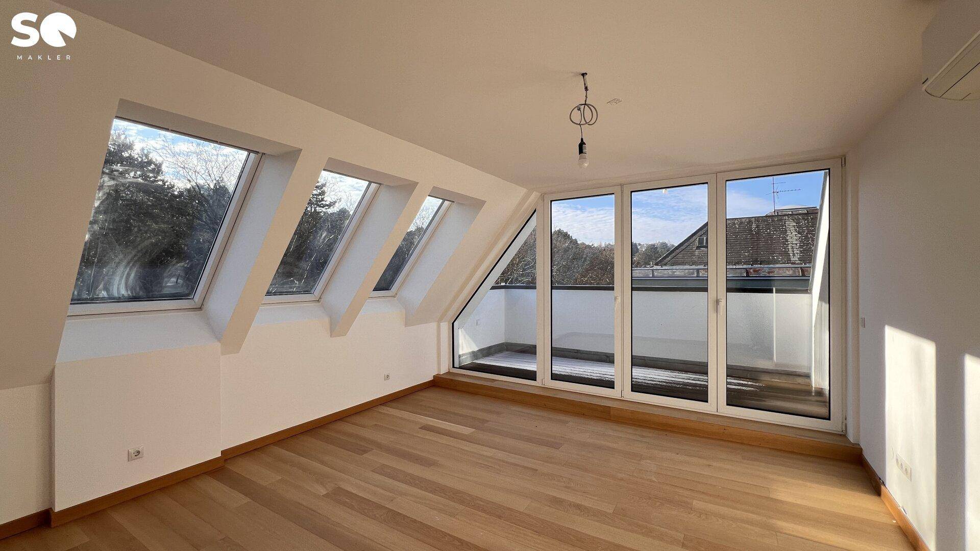 Geräumiges Zimmer mit Holzboden, mehreren Dachfenstern und Zugang zu einer Terrasse.