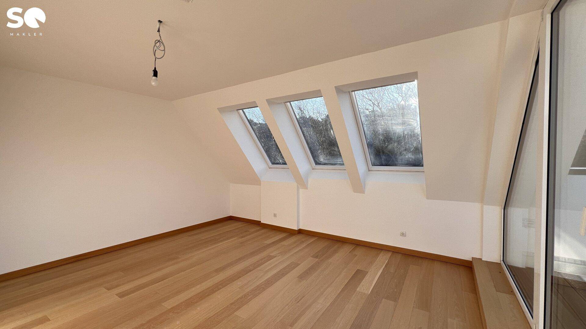 Ruhiges Zimmer im Dachgeschoss mit Holzboden und drei schrägen Dachfenstern.