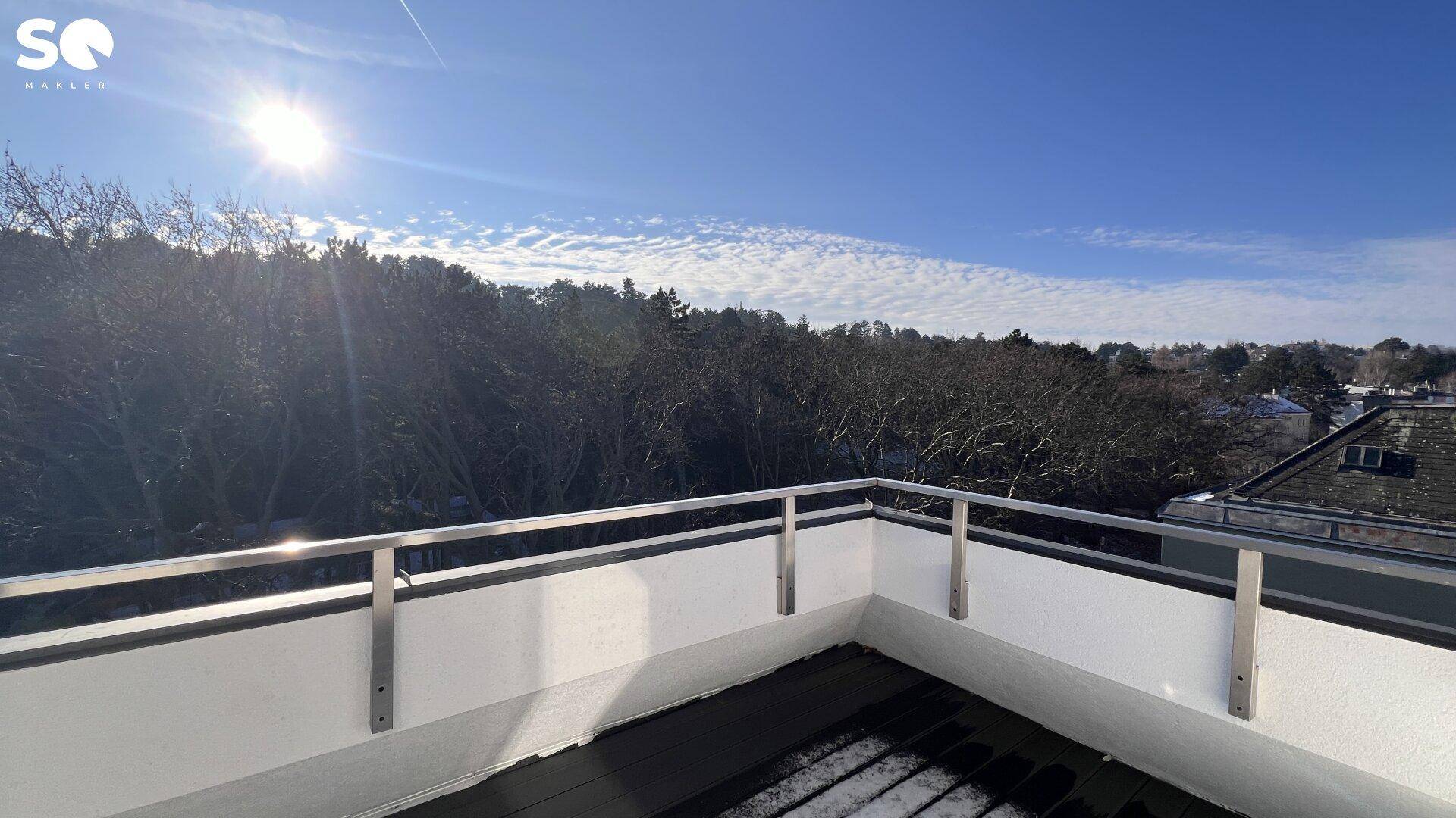 Sonniger Balkon mit Blick auf eine bewaldete Landschaft unter klarem Himmel.
